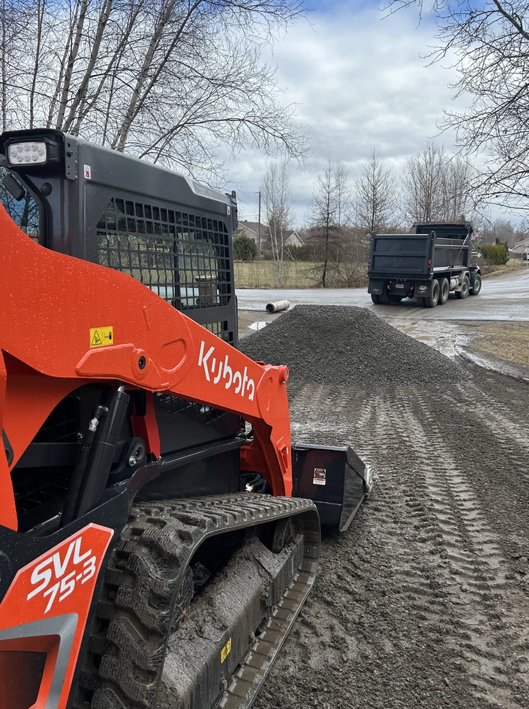Chargeuse compacte Kubota SVL75-3 devant une pile de gravier sur un chantier.